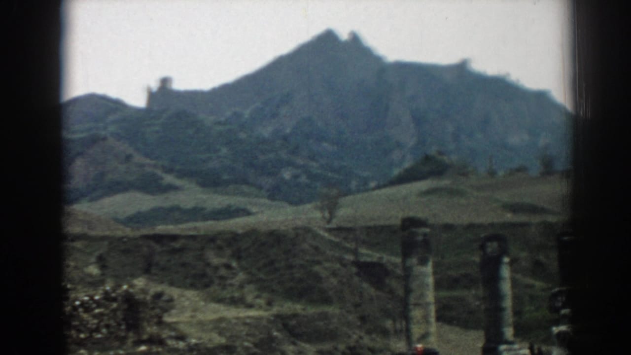A 1962 Ephesus home-movie frame shows columns and rough stonework beneath a broad hillside and jagged mountain profile.
