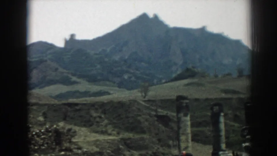 A 1962 Ephesus home-movie frame shows columns and rough stonework beneath a broad hillside and jagged mountain profile.
