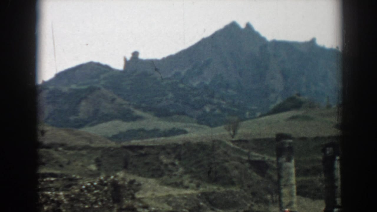 Green hills and a rocky ridge seen through dark film-frame borders.