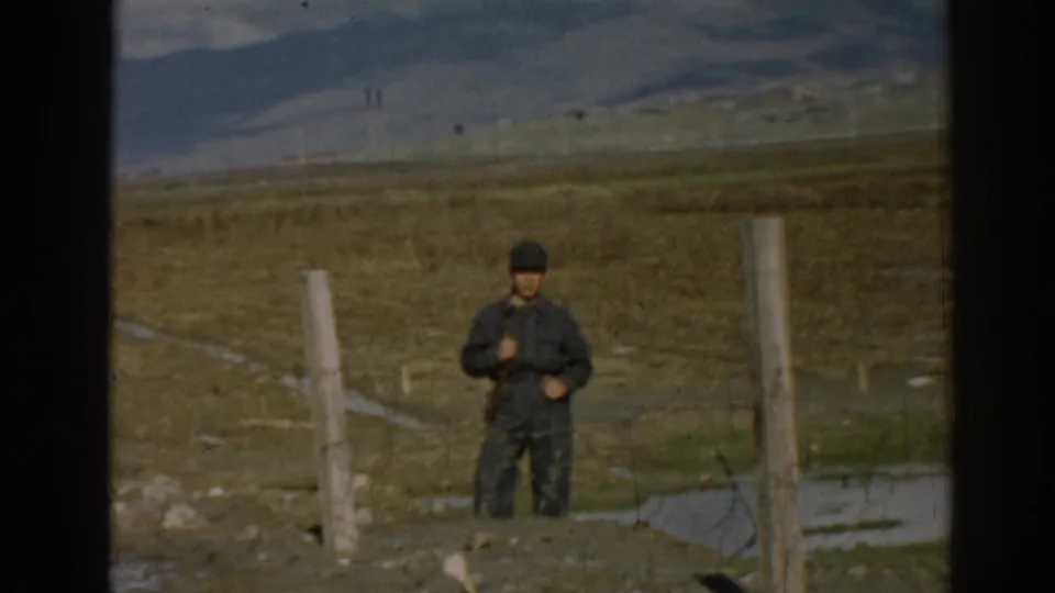 In 1962 Ephesus, Turkey footage, a man stands near fence posts in an arid field with hills behind him.