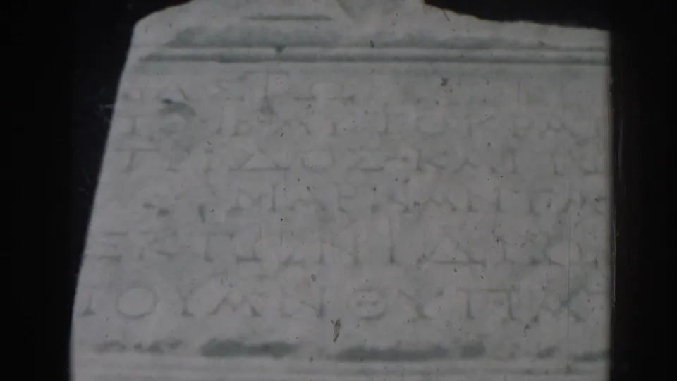 1962 Ephesus home-movie frame showing a pale inscribed stone block, soft focus, and dark film borders.