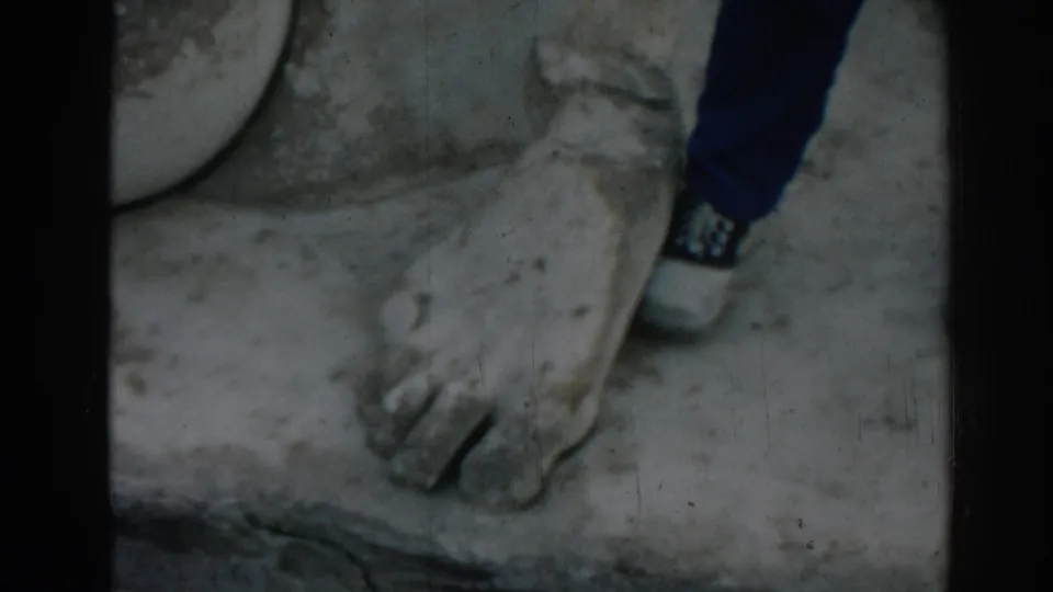 1962 Ephesus frame showing a monumental carved stone foot beside a tourist's white sneaker and blue jeans.