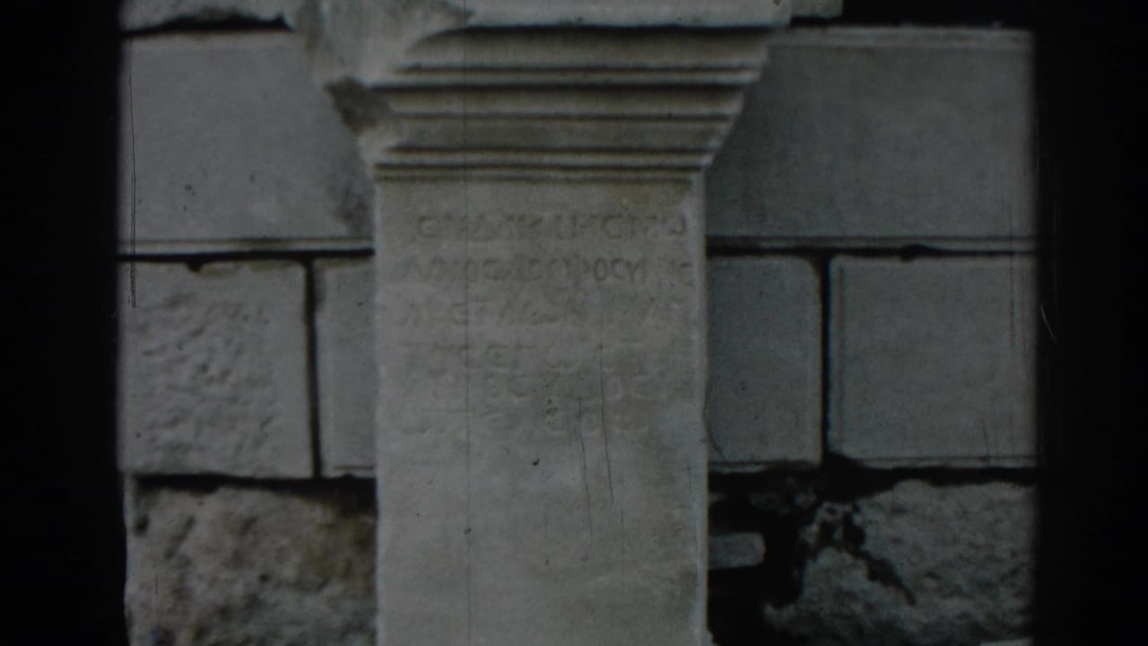 1962 8mm view at Ephesus showing a weathered stone inscription panel or column framed by surrounding masonry.