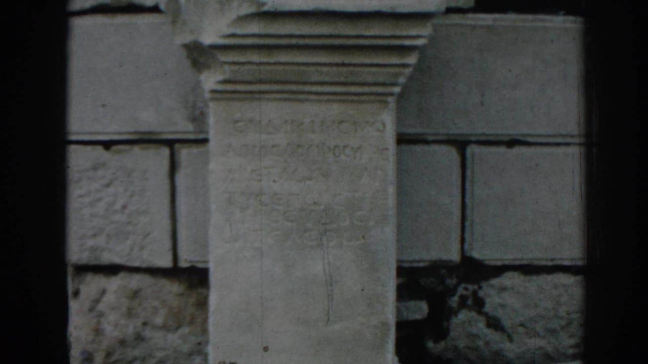 1962 Ephesus home-movie frame showing the inscription stone more fully, with block masonry and film wear visible.