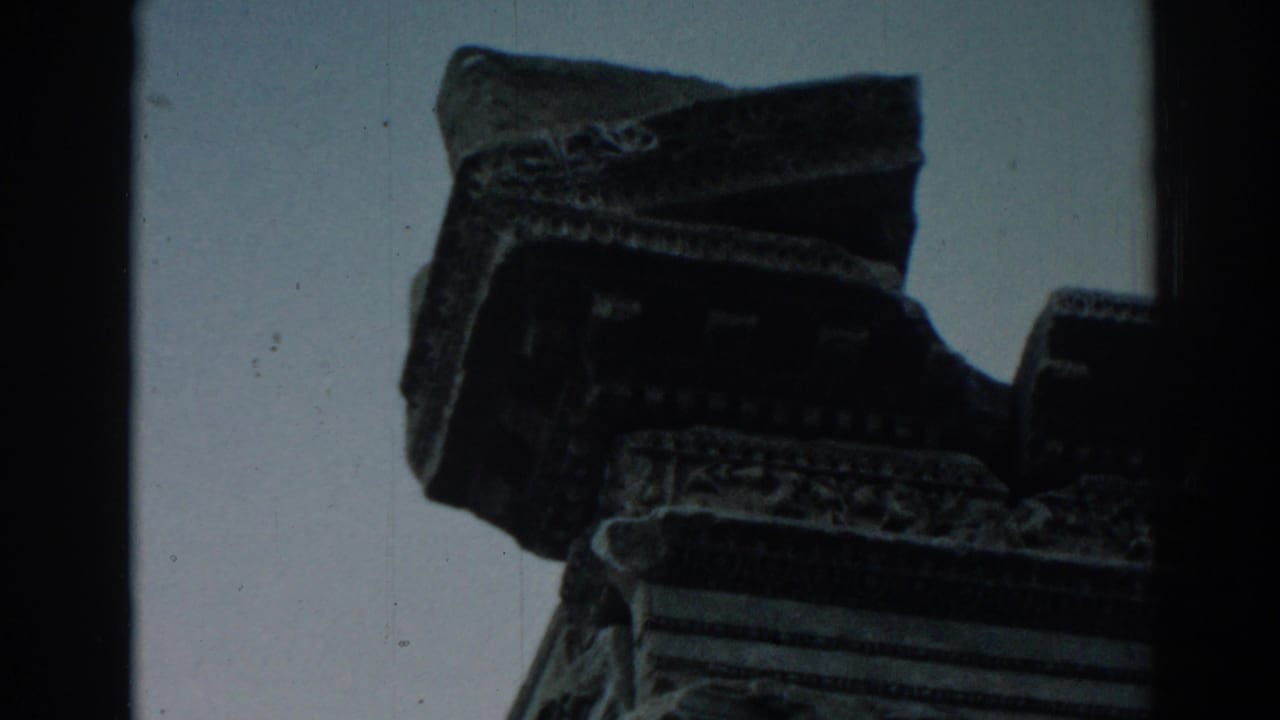 1962 8mm frame at Ephesus showing a shadowed carved ruin fragment with decorative edges against open sky.