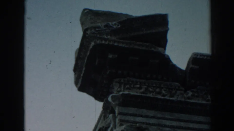 1962 8mm frame at Ephesus showing a shadowed carved ruin fragment with decorative edges against open sky.
