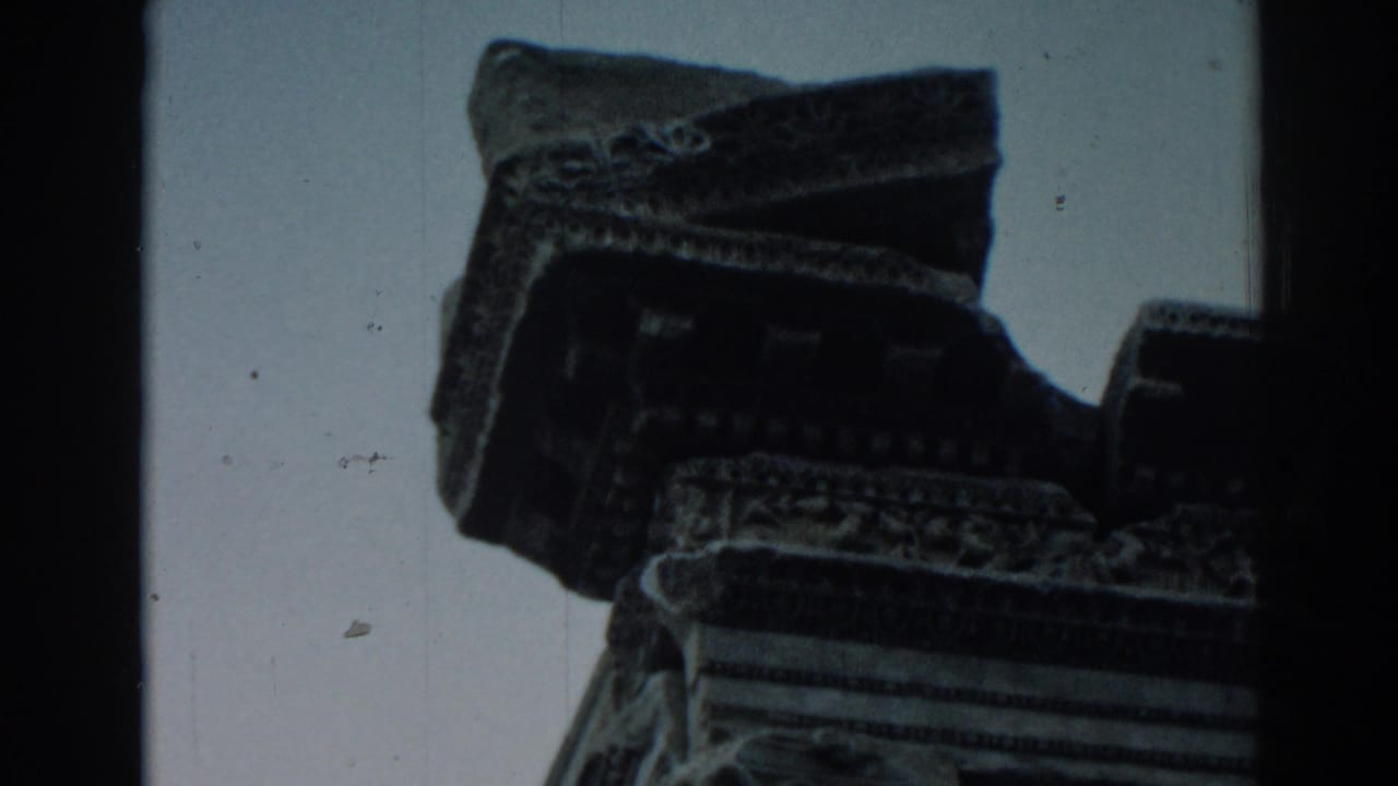 Low-angle close-up of an ornate weathered stone capital against a pale sky.