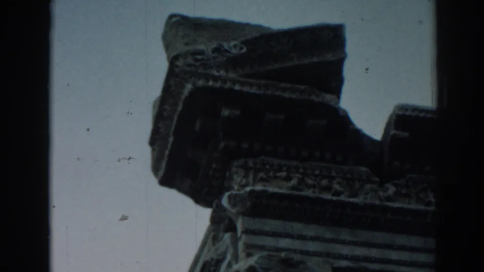 1962 Ephesus home-movie frame showing a low-angle view of carved stone architecture and a pale sky.