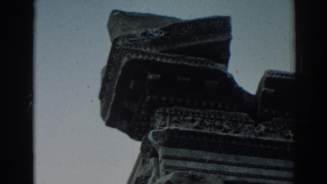 Low-angle 8mm frame from Ephesus showing weathered carved stone detail silhouetted against the sky.