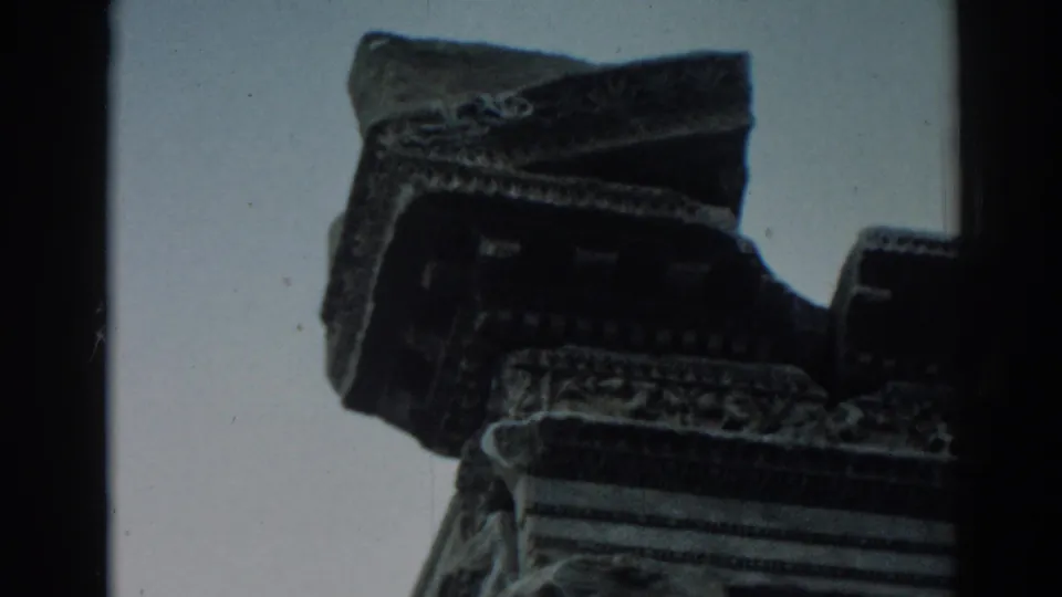 Low-angle 8mm frame from Ephesus showing weathered carved stone detail silhouetted against the sky.