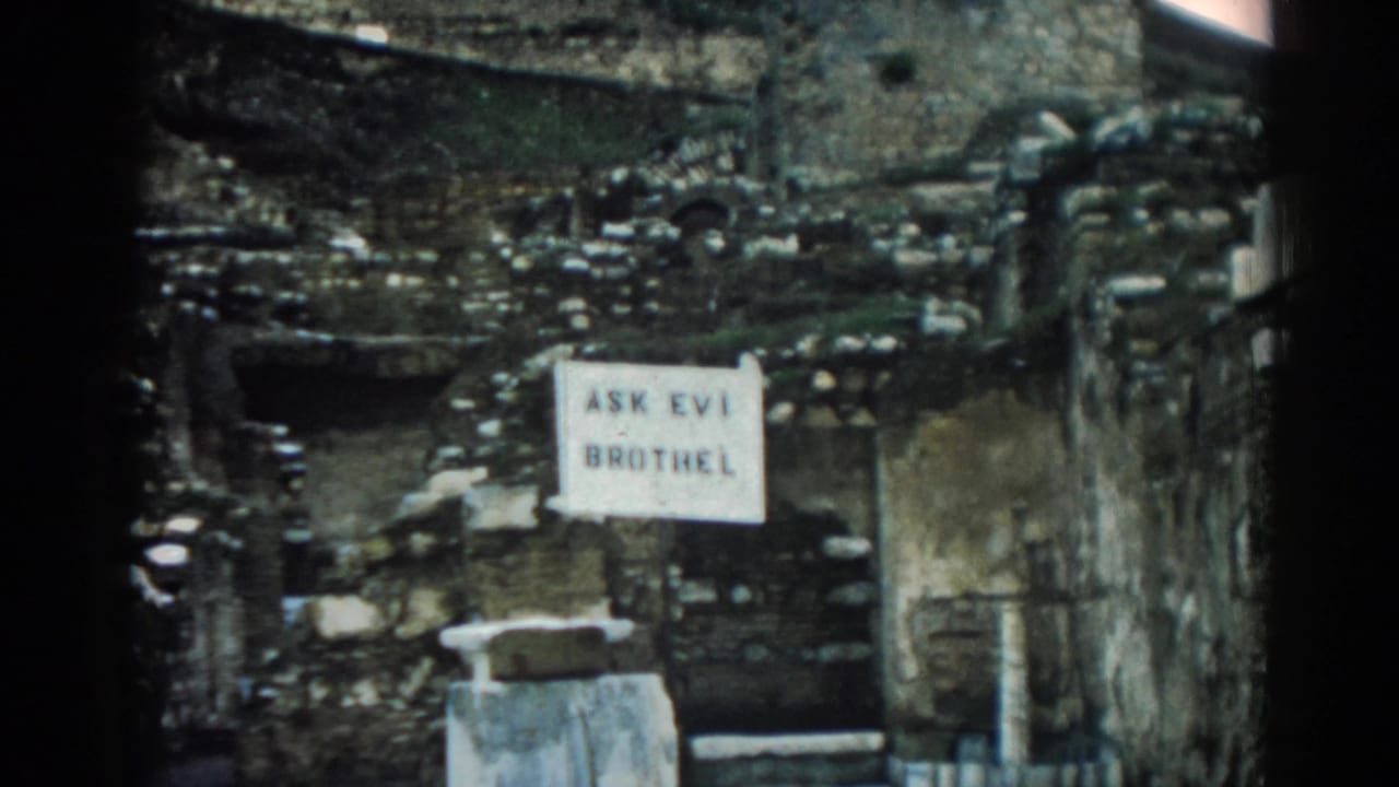 Ephesus, Turkey frame showing a white sign reading "ASK EVI BROTHEL" on a worn stone wall in 1962 8mm footage.