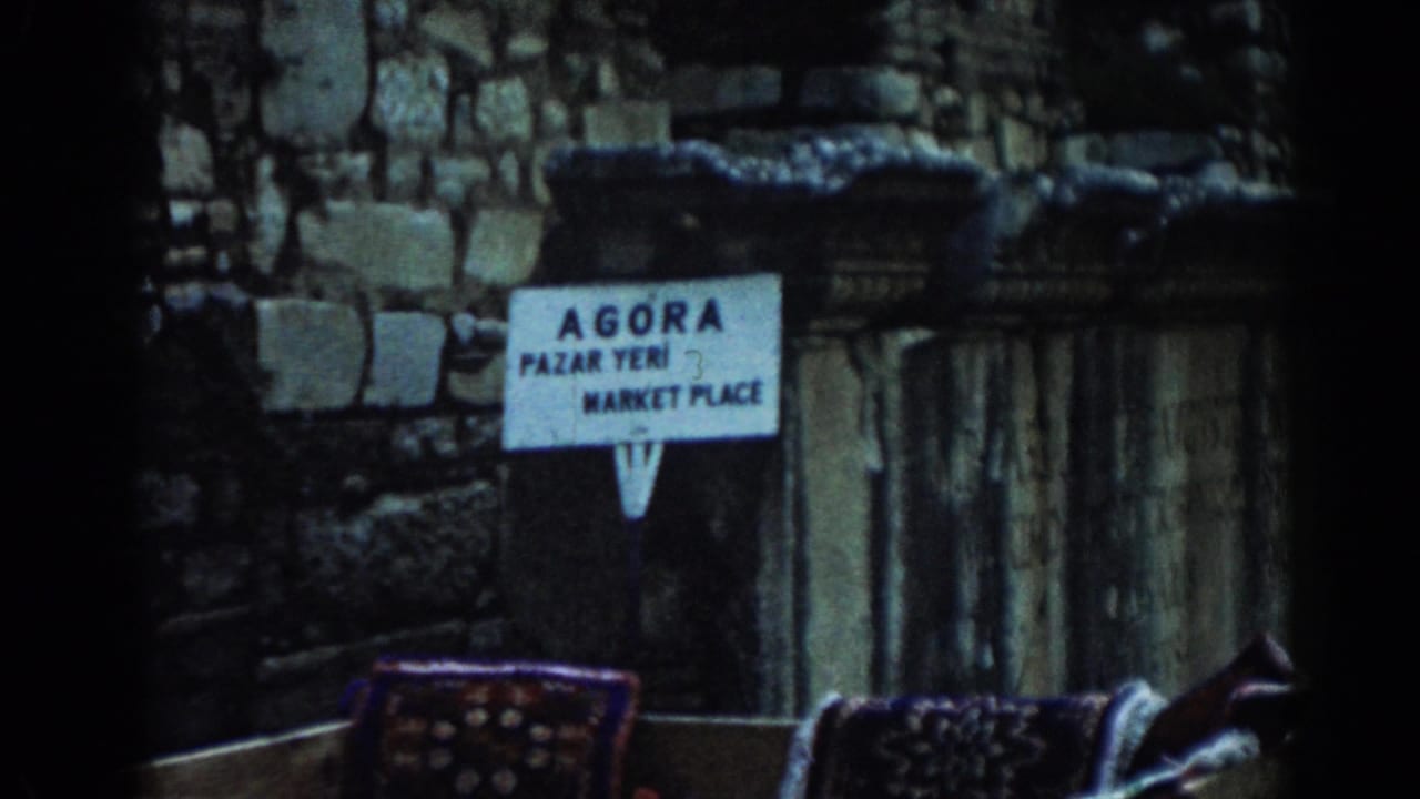 Agora marketplace sign in front of stone ruins and columns.