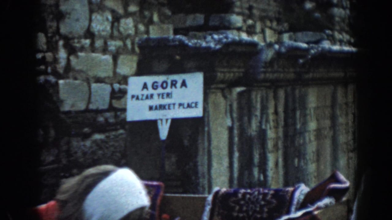1962 Ephesus travel frame with an Agora marketplace sign, ruins, and partially seen visitors wearing head coverings in the foreground.