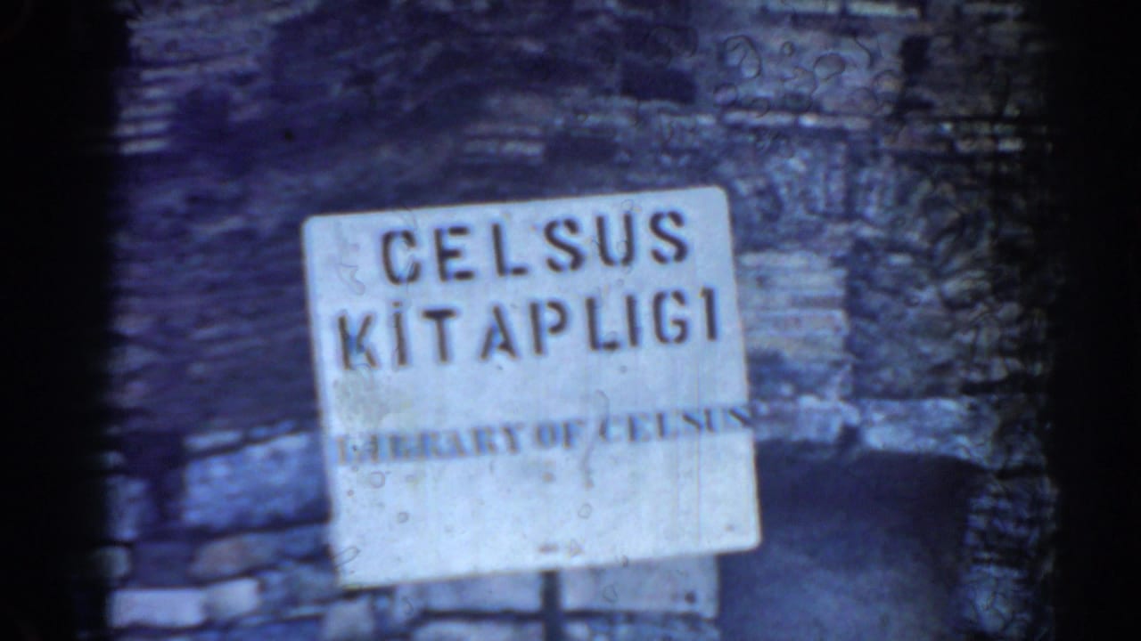 1962 Ephesus frame showing a Library of Celsus sign before weathered masonry and a dark arched opening.