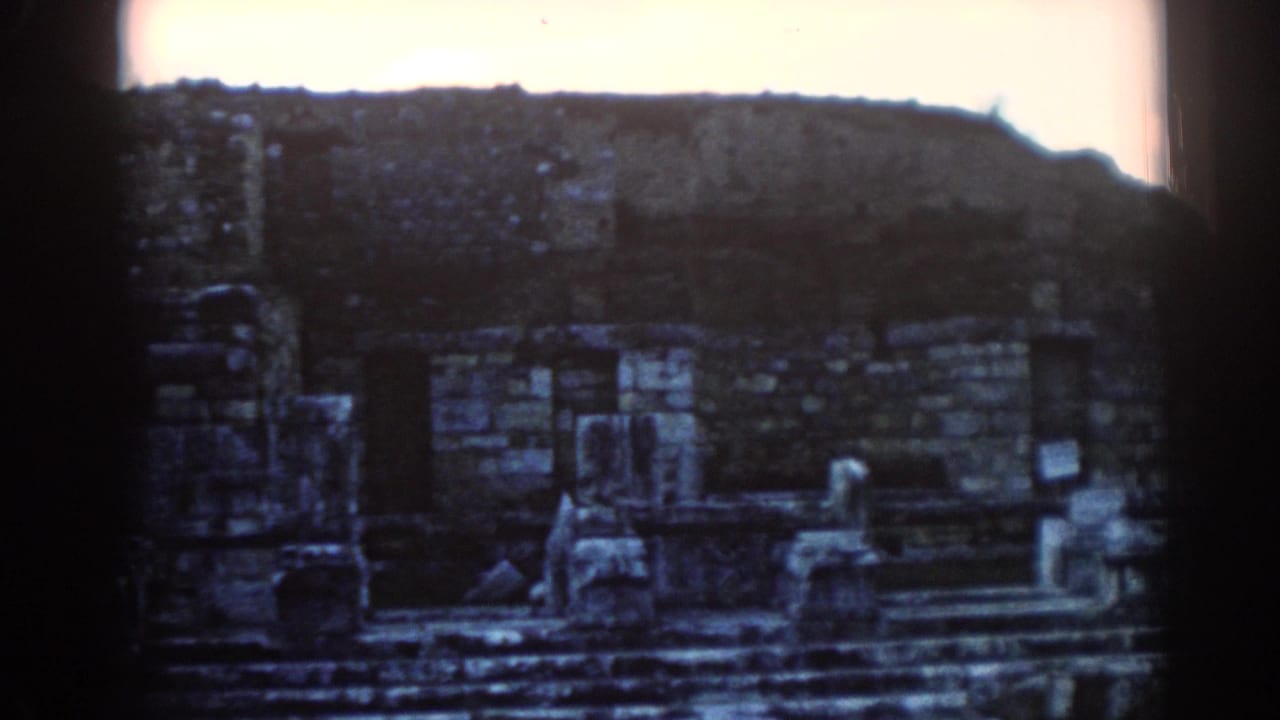 1962 Ephesus home-movie frame with stone walls, steps, and ruin fragments framed by dark 8mm borders.