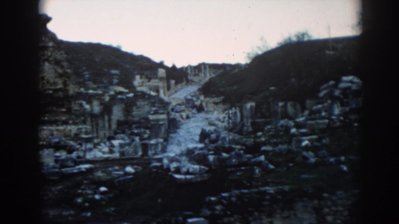 Stone path through ancient ruins with rubble, columns, and hillside in the background.