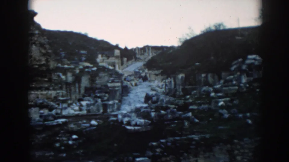 1962 Ephesus home-movie frame showing a stone path bordered by ruins, scattered masonry, and green hills.