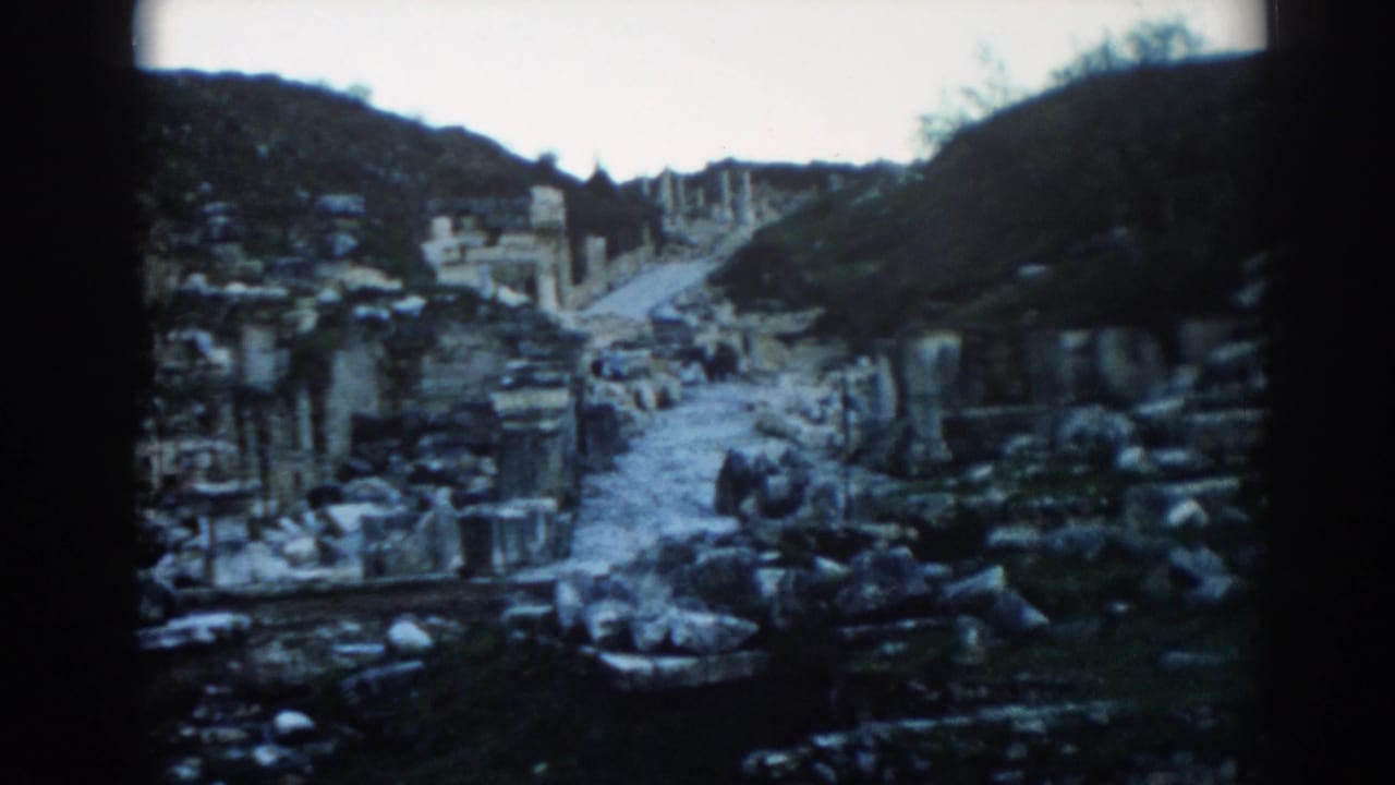 Ancient stone path with ruins and hillside vegetation, partly framed by dark film borders.