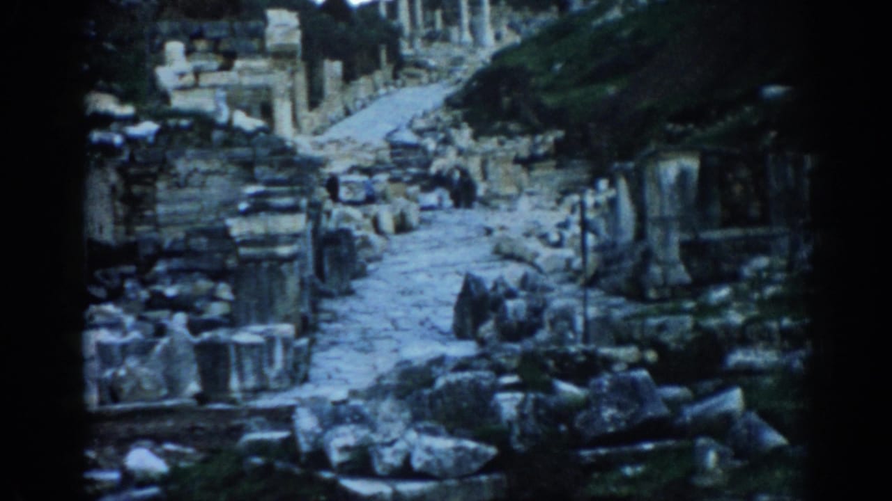Late frame from a 1962 Ephesus home movie showing a ruin-lined stone path and hillside greenery.