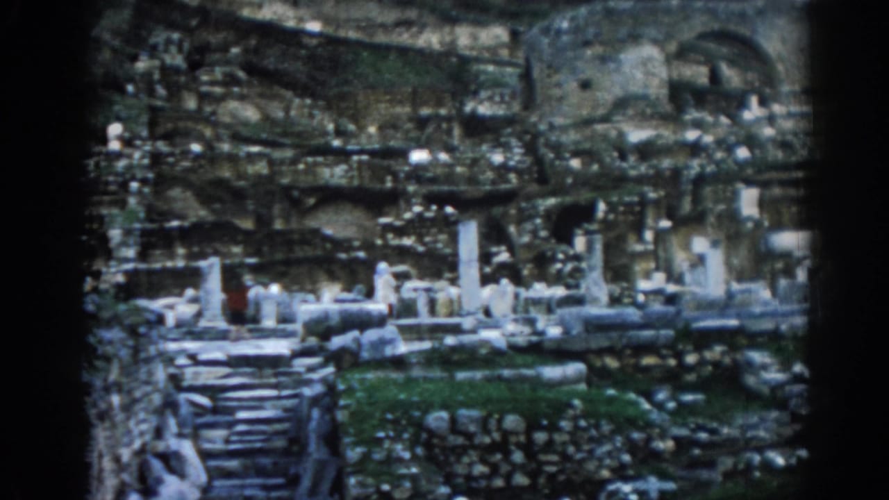 Ephesus ruins in 1962 with stone steps, partial columns, arched masonry, grass patches, and a small visitor wearing red.