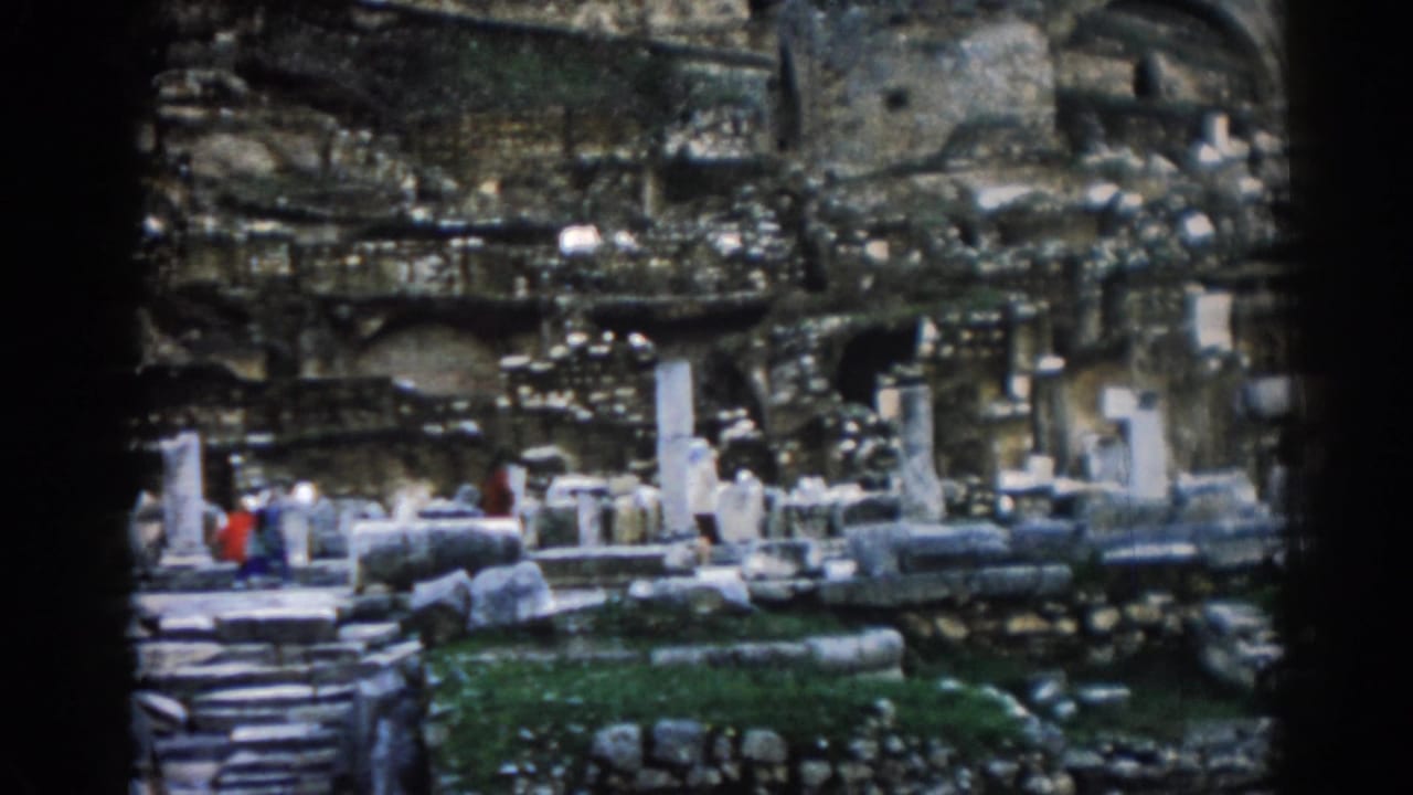 1962 Ephesus home-movie frame showing visitors moving through ancient ruins, with columns, stone steps, and weathered walls around them.