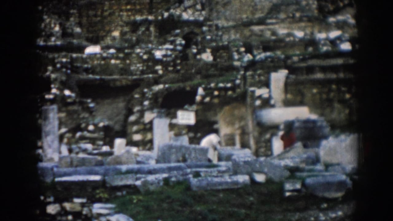 Stone ruins with columns, fragments, mossy ground, and distant visitors.