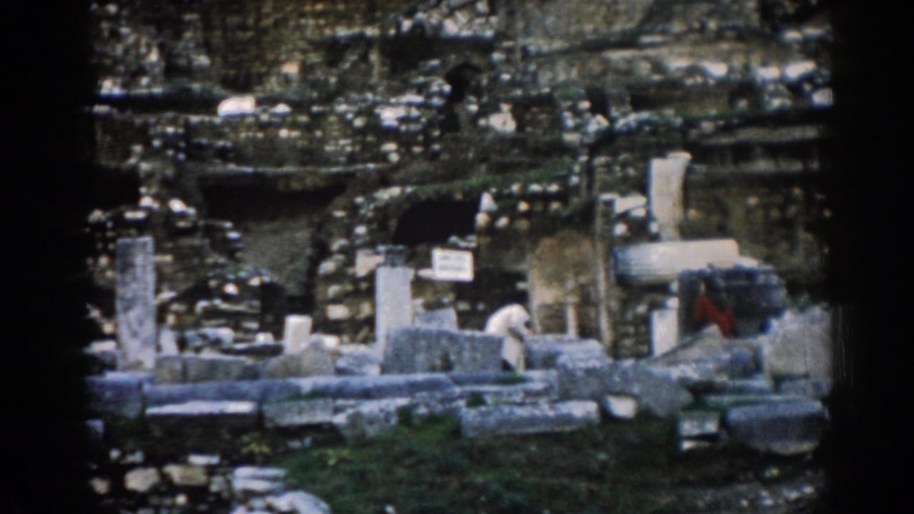 Ancient stonework with scattered blocks, columns, and visitors in white and red clothing.