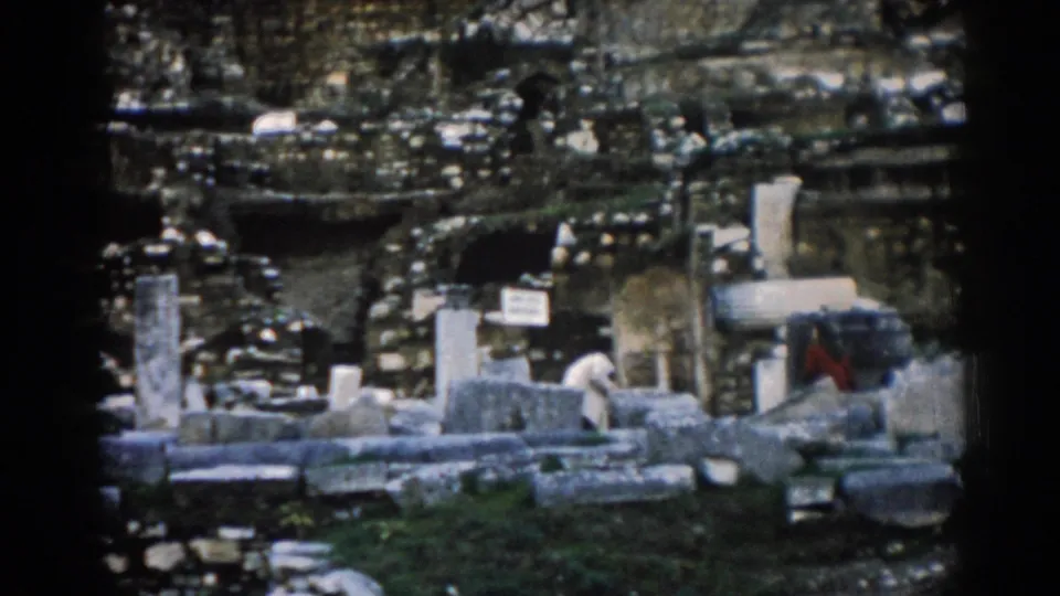Ephesus ruin view on 8mm film, showing broken stone elements, column bases, and distant visitors in light and red clothing.