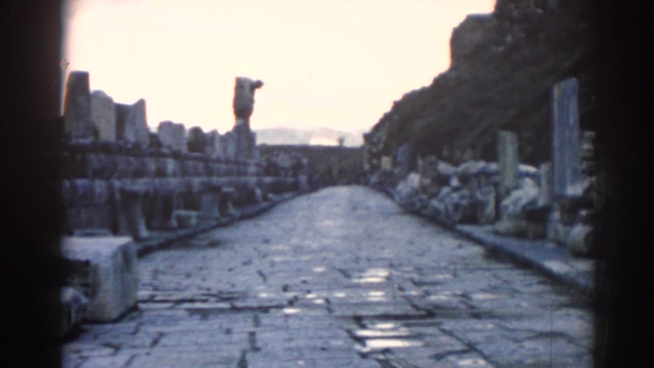 1962 Ephesus pathway view with cobblestones leading between rows of stone ruins and a distant upright statue-like form.