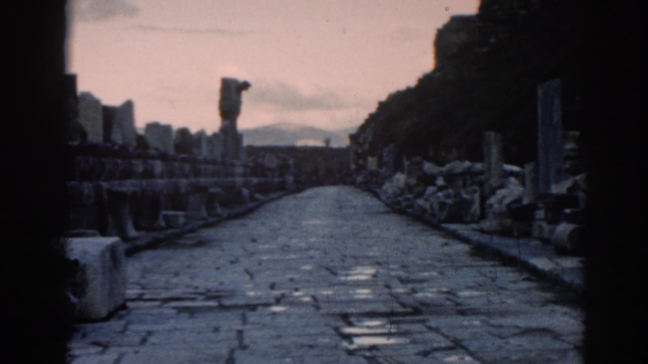 1962 8mm view along a stone road at Ephesus, Turkey, framed by ruin walls, columns, and a hazy sky.