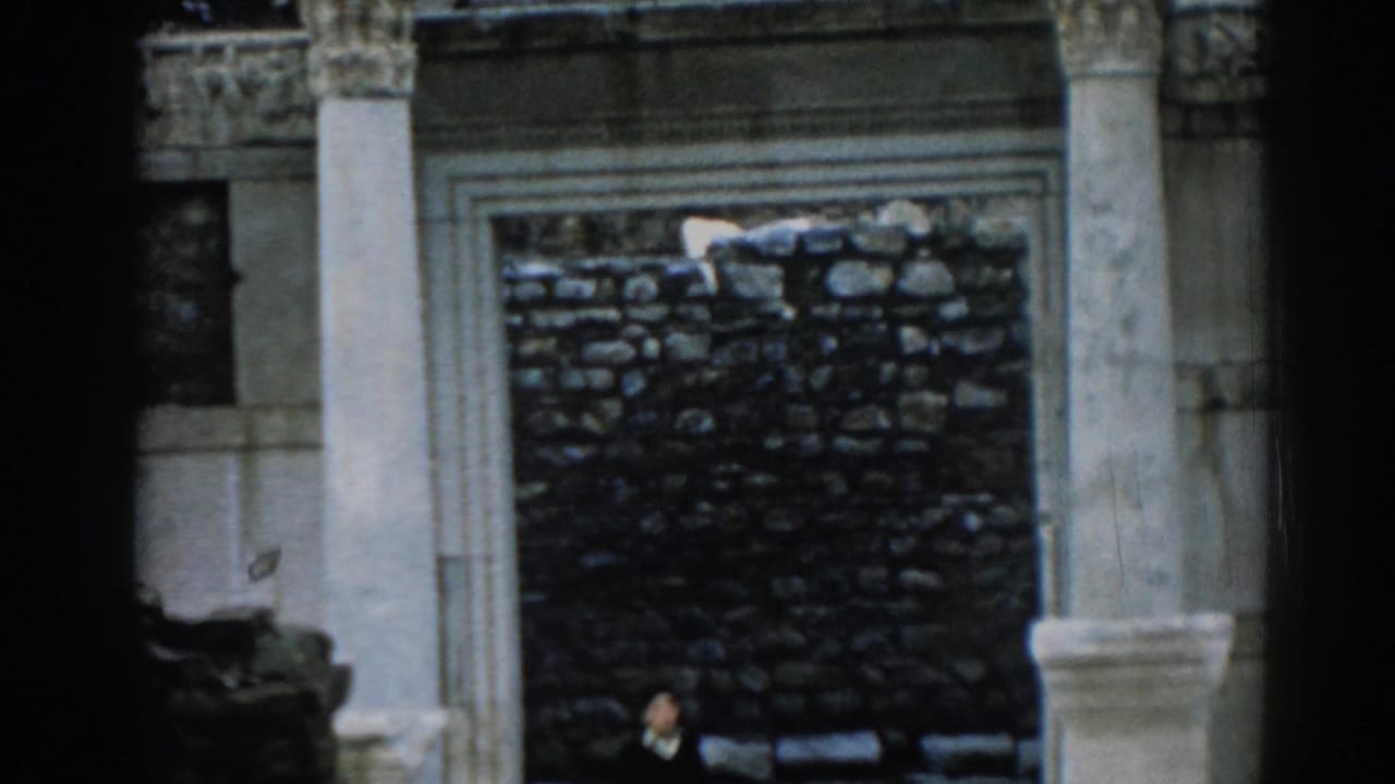 1962 Ephesus frame with pale columns around a stone wall and a small male visitor near the lower part of the ruin.