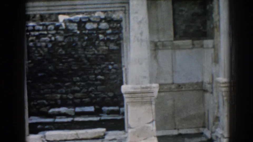 1962 Ephesus frame holding on pale architectural columns and a dark stone wall within the ancient ruin.