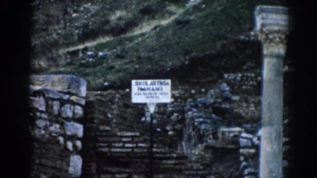1962 8mm view of Ephesus ruins with stone steps, a small site sign, rough masonry, columns, and overgrown hillside.