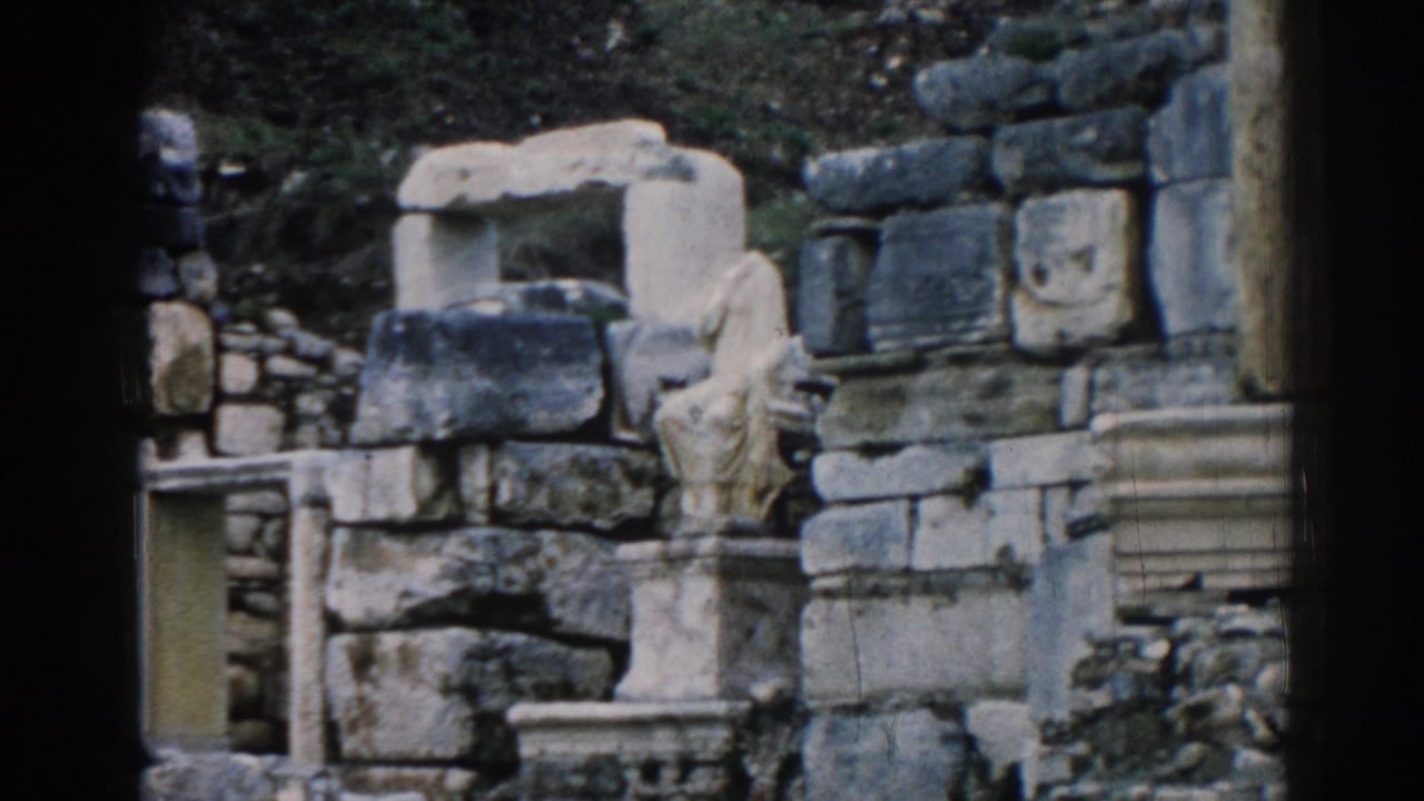1962 8mm view of Ephesus ruins with a carved statue fragment, stacked masonry, column base, and stone walls.