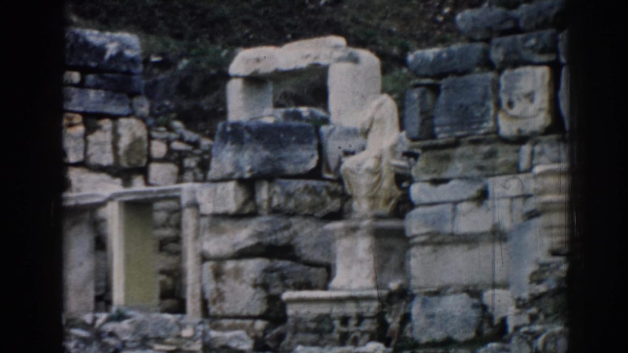 1962 Ephesus frame showing stacked stone blocks, a carved fragment, column base, and surrounding rubble in faded color.