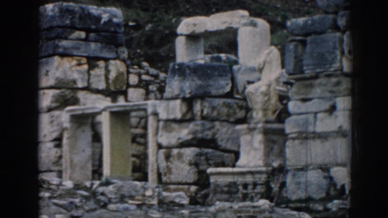 1962 8mm view of ancient stone remains at Ephesus, with stacked blocks, carved fragments, and a small opening among the ruins.