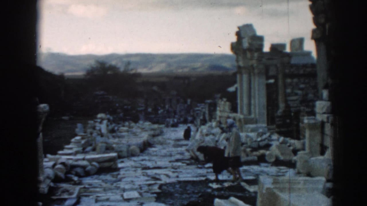 Ancient ruin path with columns, scattered stones, and visitors walking in the distance.