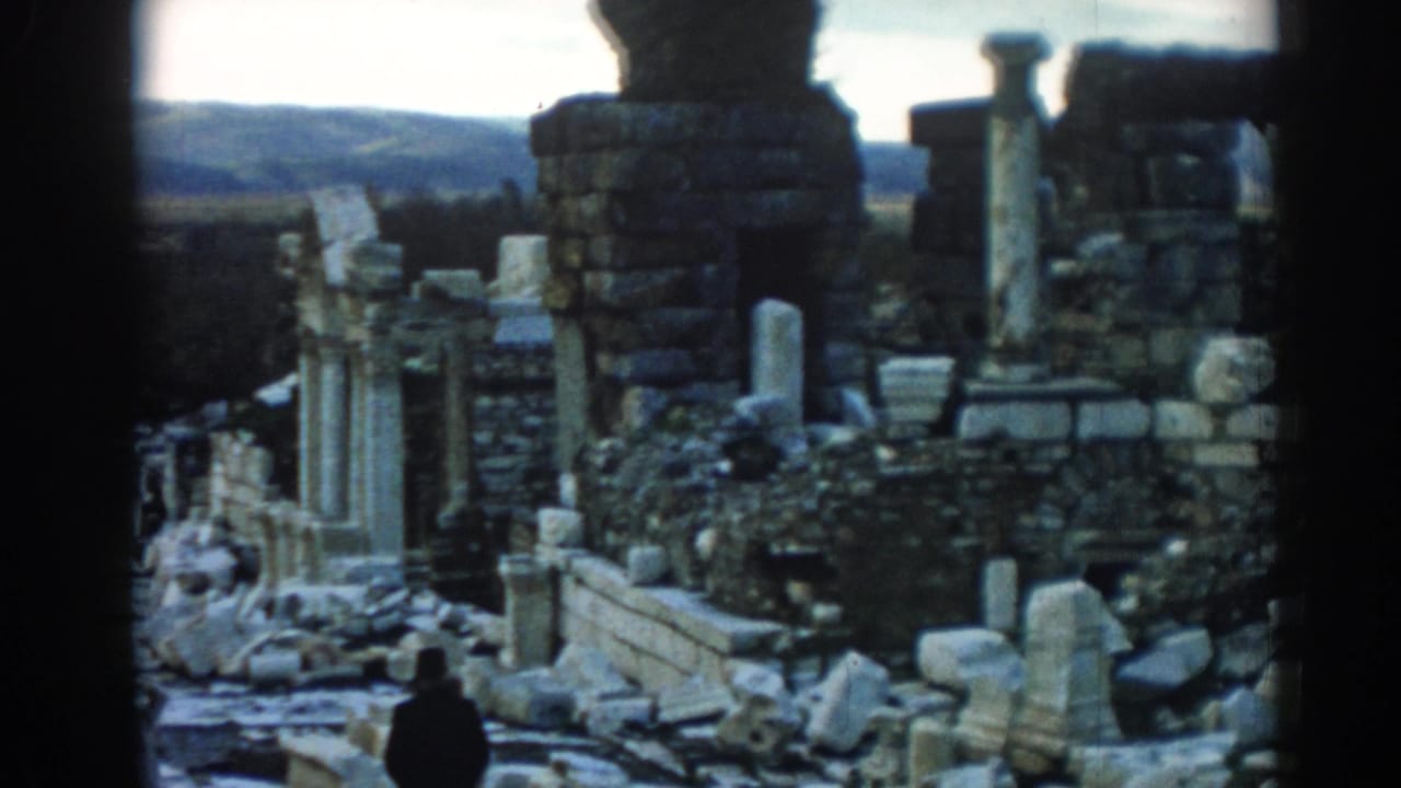 1962 8mm frame at Ephesus showing a visitor among ancient stone walls, columns, broken blocks, and distant hills.