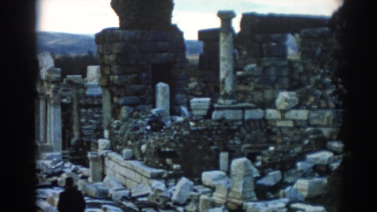 1962 Ephesus travel-film frame with a distant visitor beside weathered columns, broken stonework, and scattered ruins.