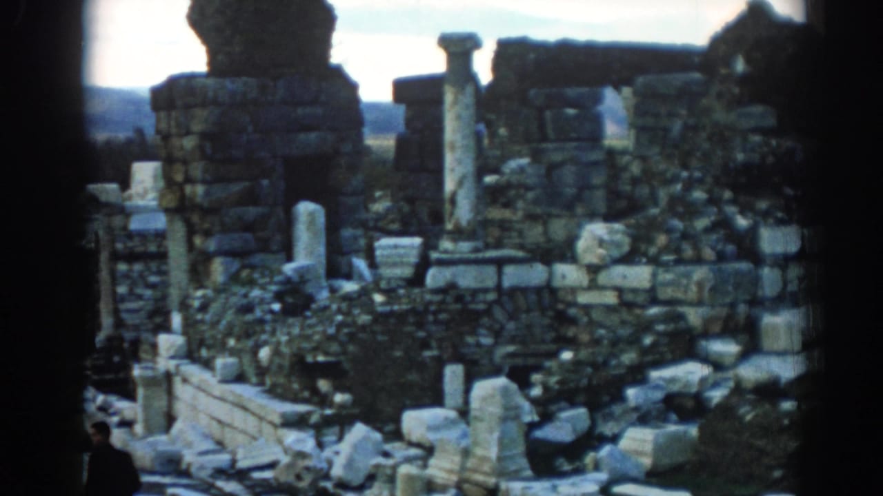8mm home-movie view of Ephesus ruins in 1962, with columns, masonry, scattered fragments, and a partially seen visitor.