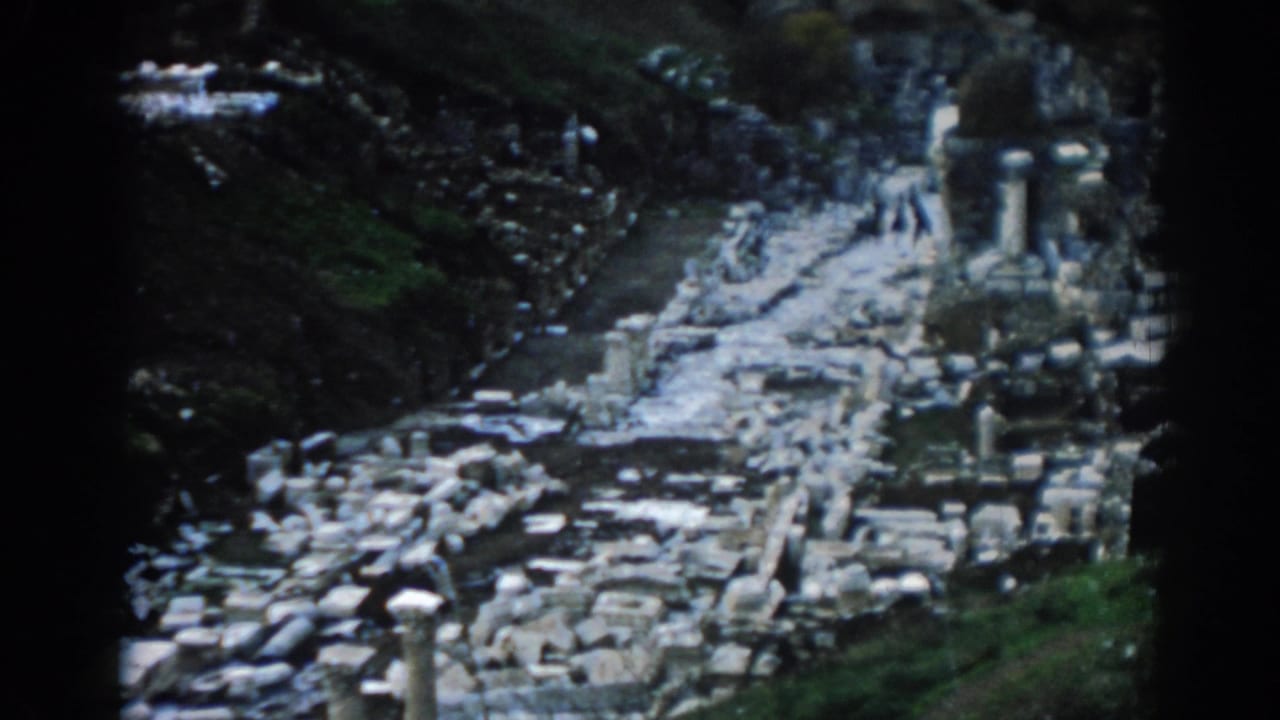 Soft 8mm frame from Ephesus, Turkey, with weathered ruins, upright columns, green slopes, and visitors on the path.