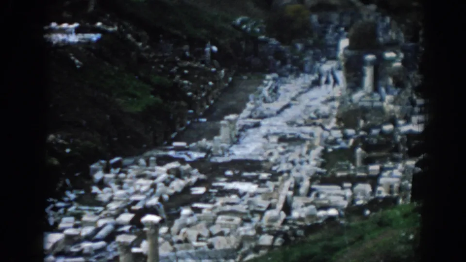 Soft 8mm frame from Ephesus, Turkey, with weathered ruins, upright columns, green slopes, and visitors on the path.