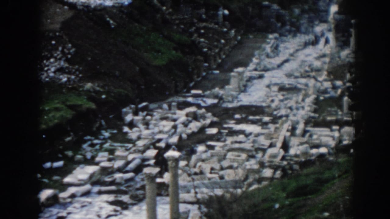 1962 Ephesus travel footage showing a visitor among scattered columns, stone blocks, and grassy embankments.