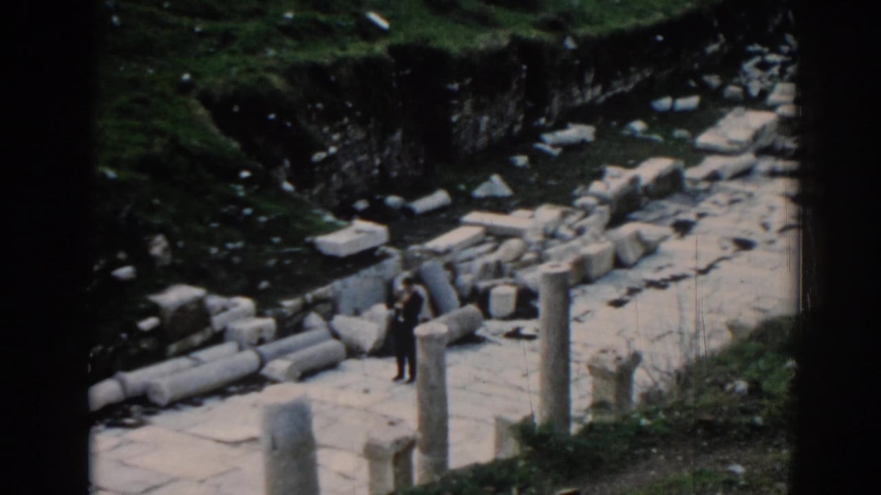 A visitor in dark clothing stands near upright columns and broken stones in 1962 home-movie footage from Ephesus.
