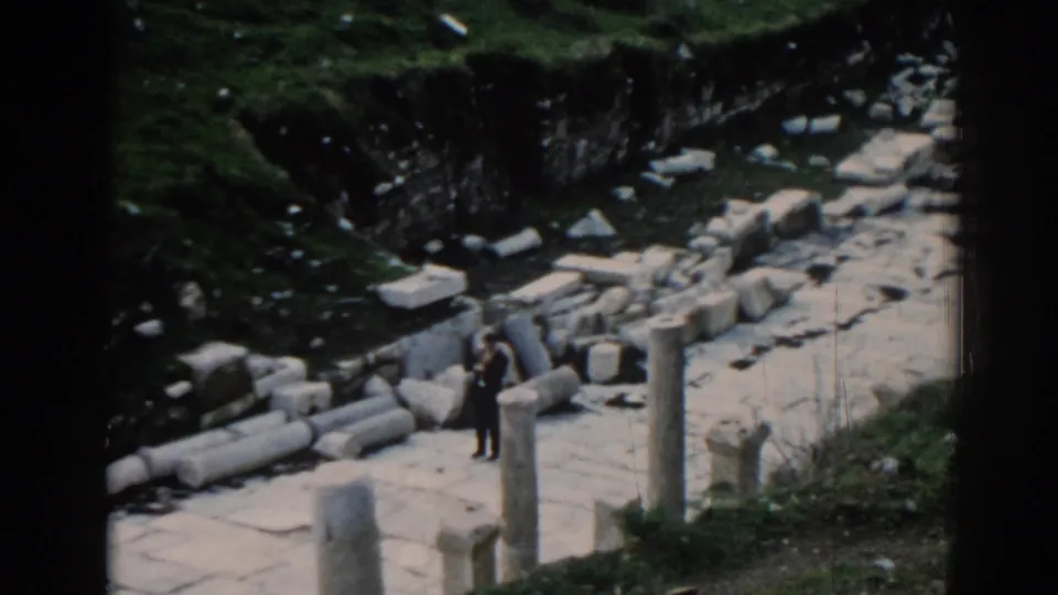 A visitor in dark clothing stands near upright columns and broken stones in 1962 home-movie footage from Ephesus.