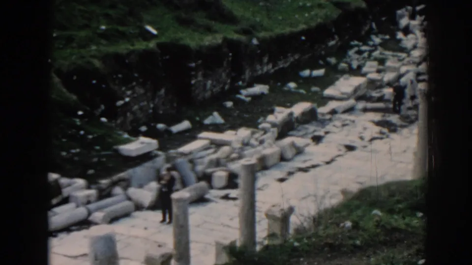 1962 Ephesus home-movie frame showing tourists among scattered stone blocks, columns, and grassy edges.