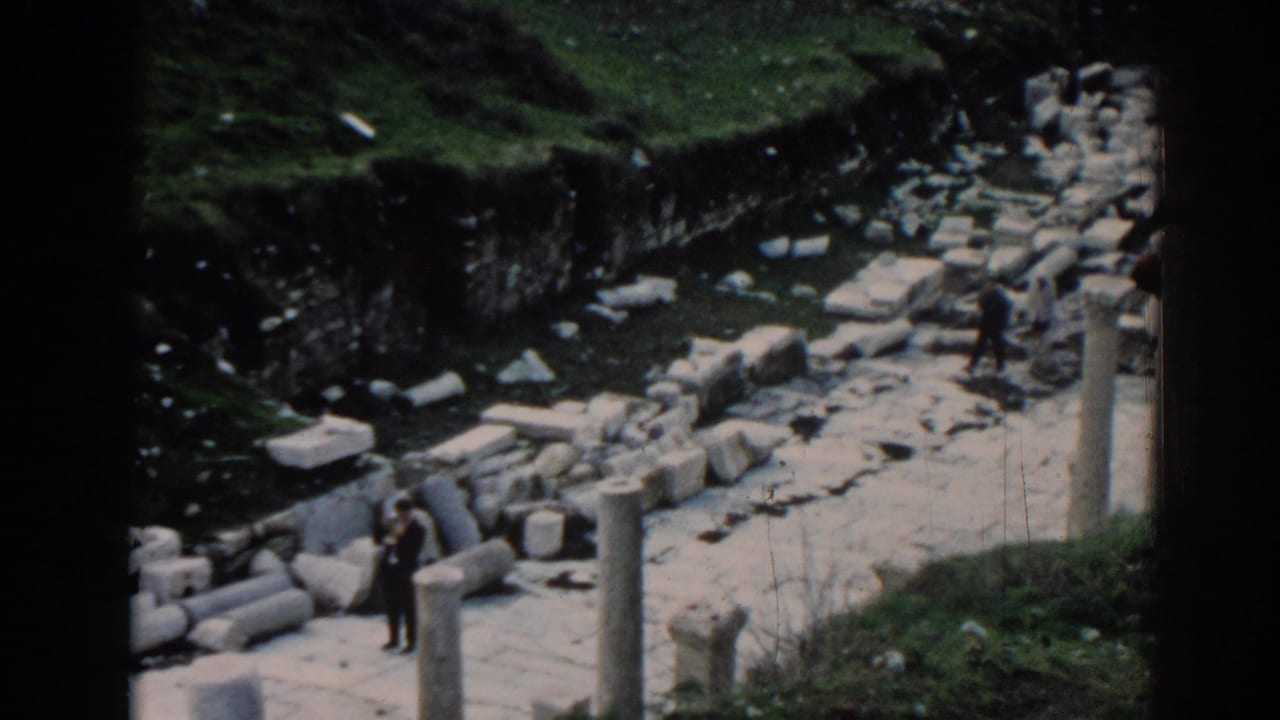 A few visitors walk through scattered stones beside upright columns.