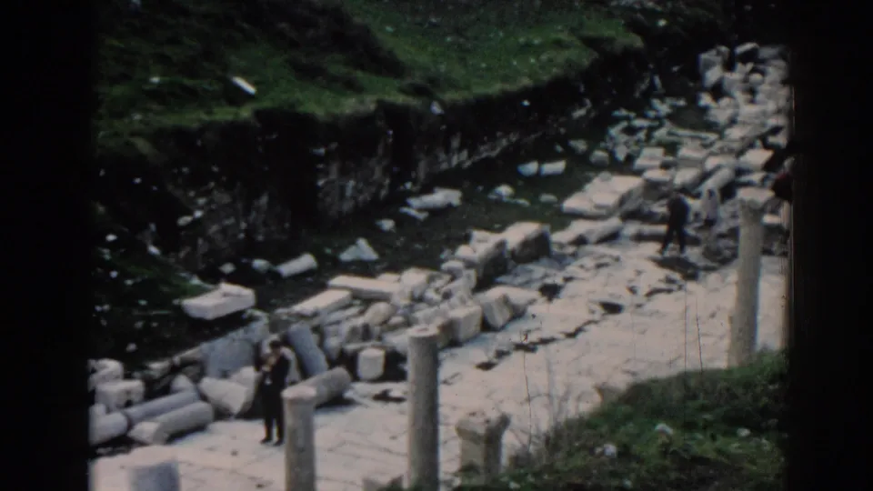 Visitors move through the Ephesus ruins in a soft 8mm frame with fallen masonry and green ground cover.