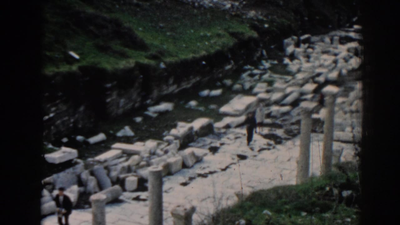 Soft 8mm frame of the Ephesus ruins with tourists dispersed among stone blocks, columns, and grassy banks.