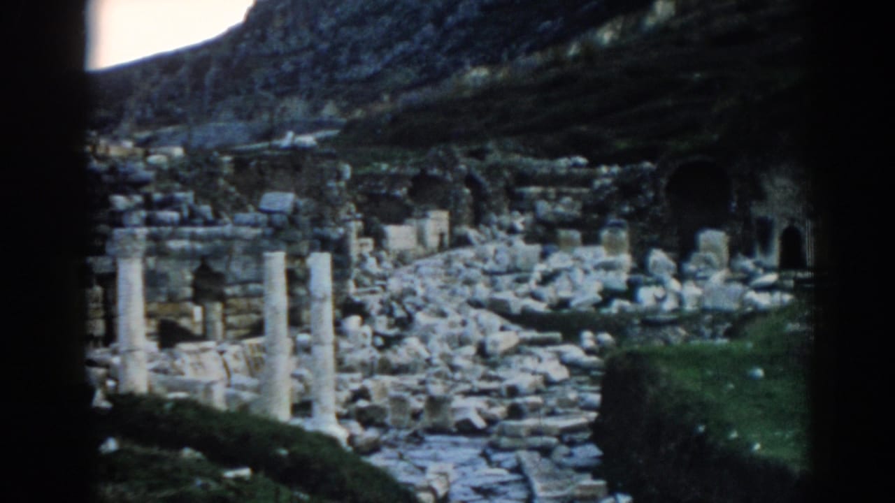 Late frame from the 1962 Ephesus 8mm clip, showing upright columns, scattered masonry, and shadowed hillside ruins.